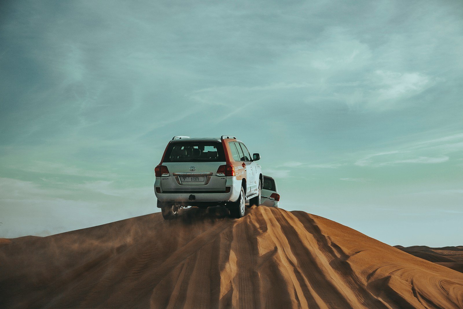 a white car driving on top of a sandy hill